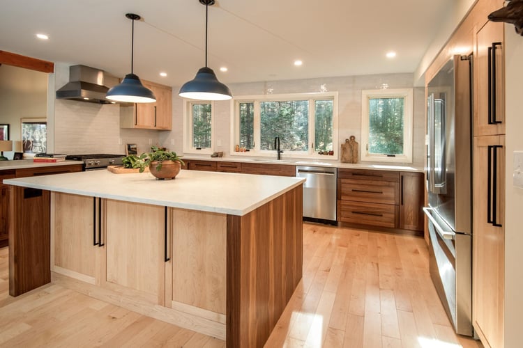 Angled view of a modern kitchen remodel in Hollis, NH, by Blackdog Design/Build/Remodel, highlighting an oversized island with a white quartz countertop, walnut cabinetry, pendant lights, and abundant natural light.