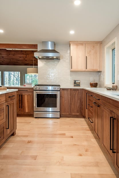 Cooking area in a modern kitchen remodel in Hollis, NH by Blackdog Design/Build/Remodel with walnut base cabinets, light maple upper cabinets, white subway tile backsplash, and stainless steel range and vent hood.