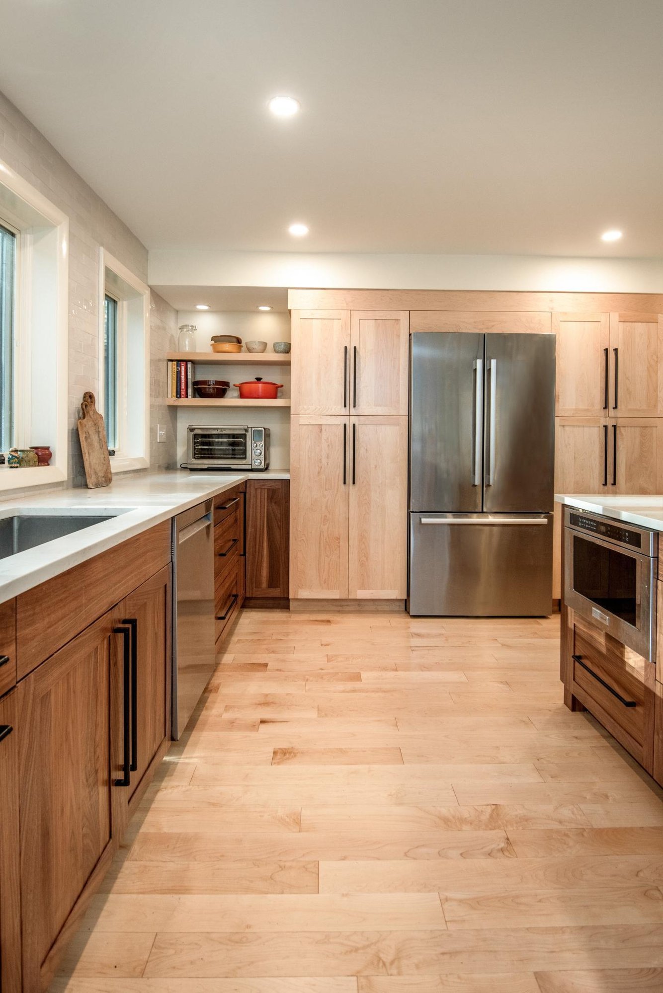 Modern kitchen remodel in Hollis, NH by Blackdog Design/Build/Remodel showing built-in refrigerator, light maple pantry cabinets, walnut base cabinets, white countertops, and light hardwood flooring.