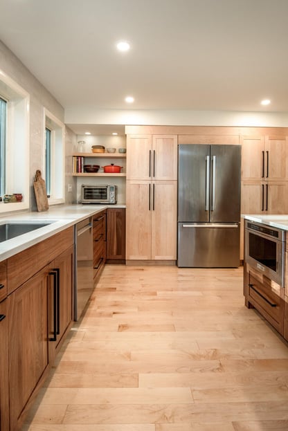Modern kitchen remodel in Hollis, NH by Blackdog Design/Build/Remodel showing built-in refrigerator, light maple pantry cabinets, walnut base cabinets, white countertops, and light hardwood flooring.