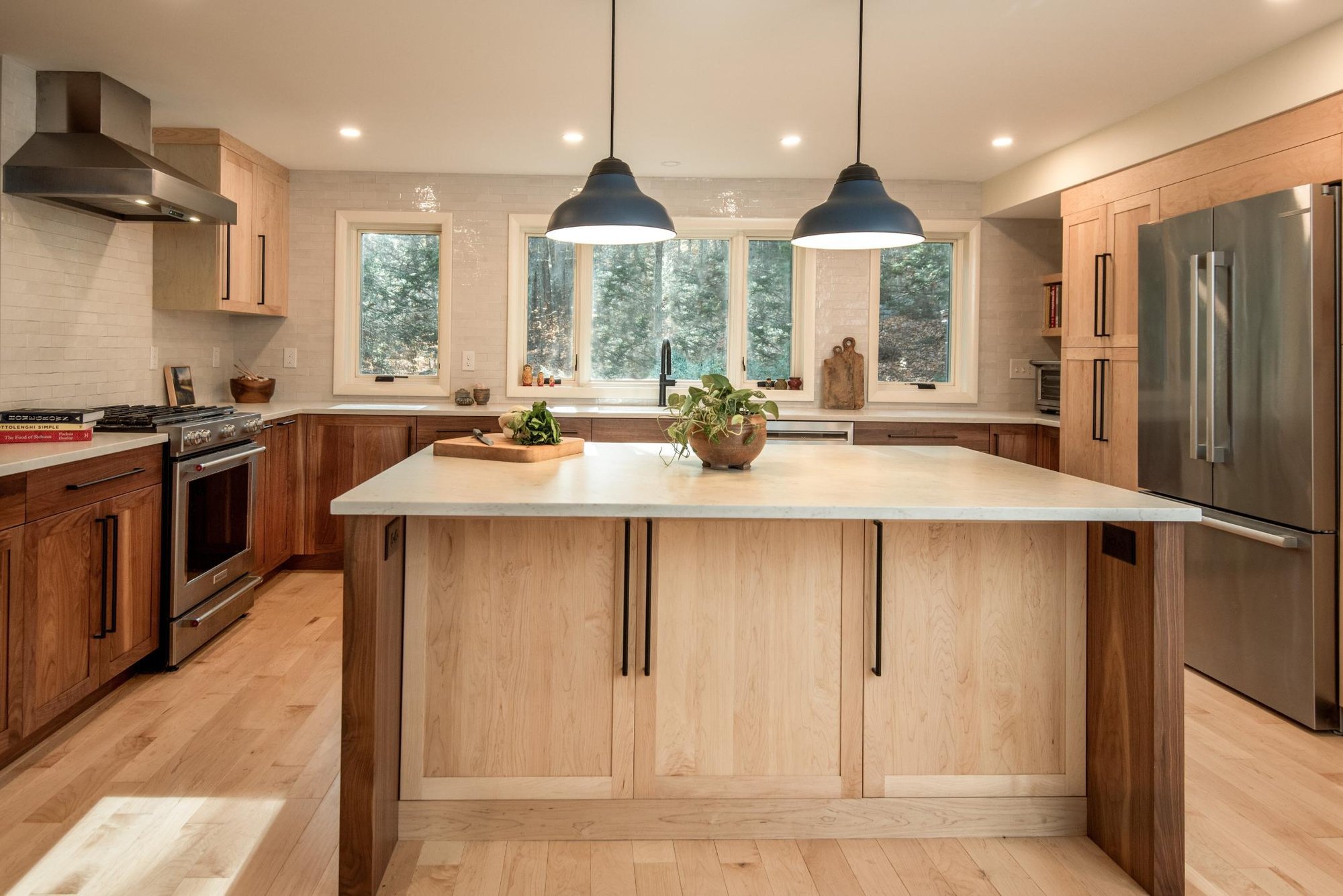 Wide view of a modern kitchen remodel in Hollis, NH, by Blackdog Design/Build/Remodel, highlighting an oversized island with a white quartz countertop, walnut cabinetry, pendant lights, and abundant natural light.