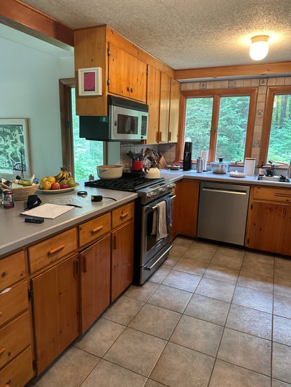 Original kitchen layout in Hollis, NH, by Blackdog Design/Build/Remodel showing wood cabinets, tiled backsplash, stainless steel appliances, and sink centered under large windows.