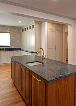 Remodeled kitchen with wood floors, woodgrain island with black/gray stone countertop and small sink in the middle with brushed gold faucet.