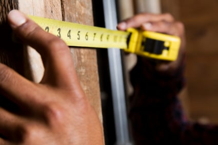 A pair of hands holding a tape measure up against wood.