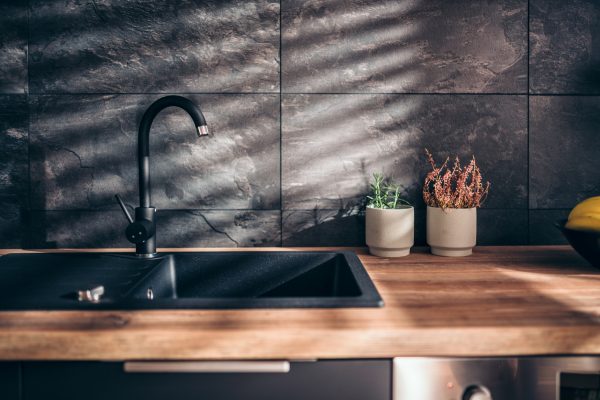 Modern kitchen with butcher block countertop, matte black sink and faucet, and matte black large tile backsplash.
