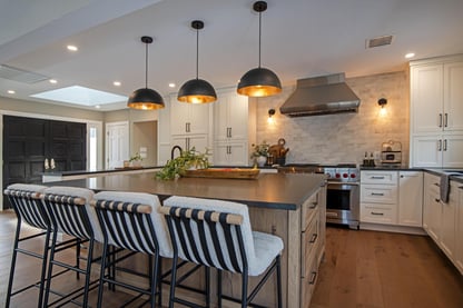 A kitchen remodel in Andover, MA by Blackdog Design/Build/Remodel featuring white shaker cabinets, a large square center island with seating, black pendant lights, and stainless steel appliances