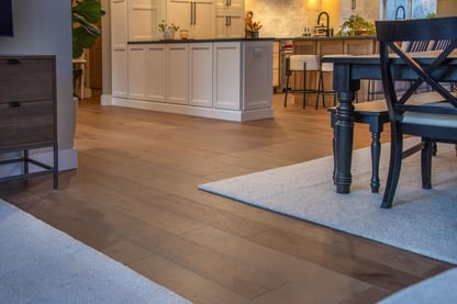 A view featuring wide-plank wood flooring looking beyond the dining table and onto the kitchen from the living room in a remodeled home by Blackdog Design/Build/Remodel