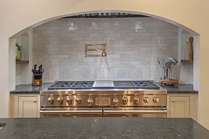 A stainless steel range underneath a custom archway and tile backsplash in a remodeled kitchen by Blackdog Design/Build/Remodel in Andover, MA