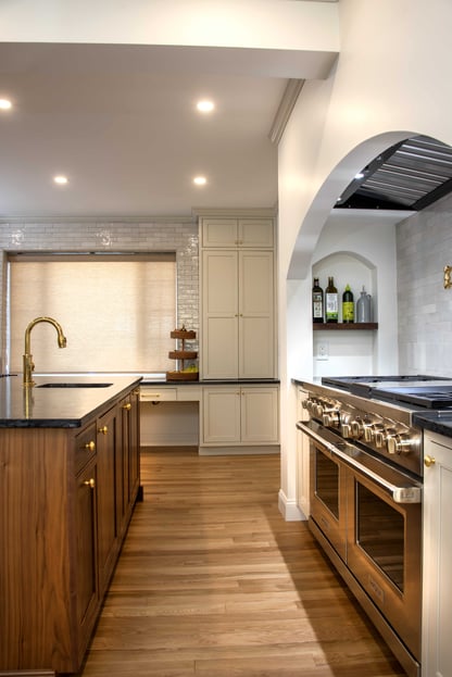 A kitchen remodel in Andover, MA featuring a large wood island with a prep sink opposite of an industrial stainless steel range underneath a custom archway and subway tile backsplash.