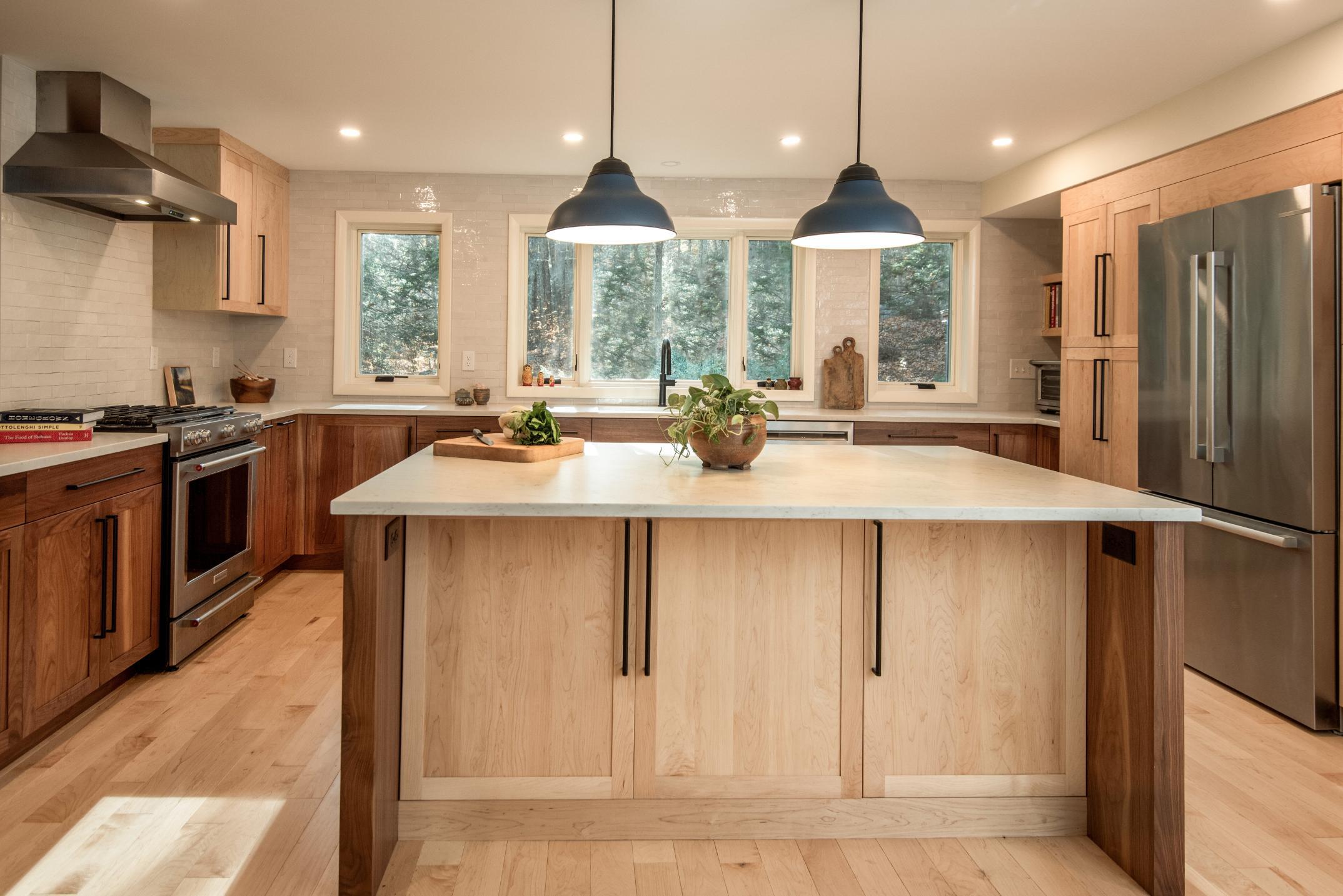 Wide view of a modern kitchen remodel in Hollis, NH, by Blackdog Design/Build/Remodel, highlighting an oversized island with a white quartz countertop, walnut cabinetry, pendant lights, and abundant natural light.