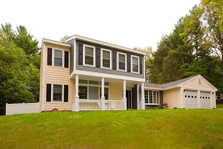 Updated two-toned yellow and dark gray siding on Colonial-style house with trees in background