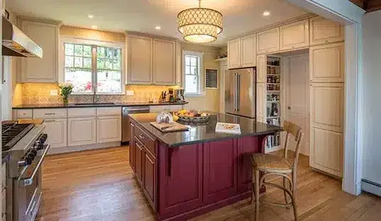 Blackdog kitchen remodel with red cabinets for small square island in the middle with black stone countertop. White cabinets against wall, wood floors.
