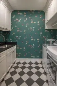 Laundry room with black and white diamond design tile flooring, green accent wall with small design on it, white cabinets, a single sink, and laundry machines on the right.