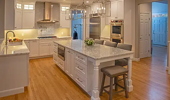 Large updated kitchen with a kitchen island, white cabinets, light gray/white stone countertops. Wood floors. Pendant lighting.