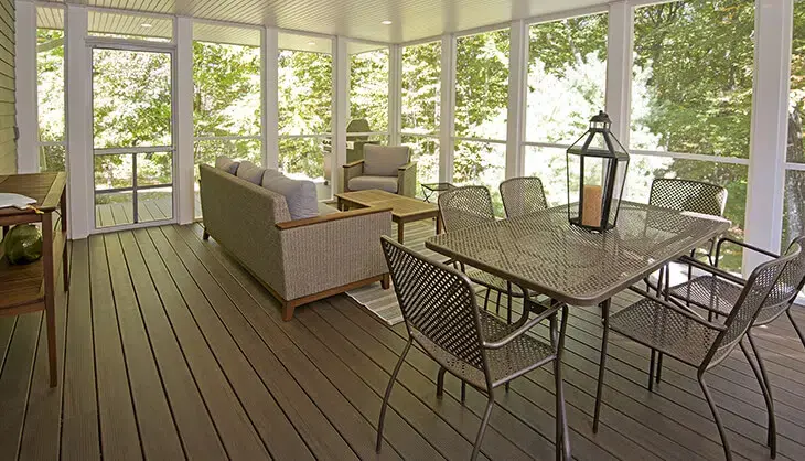 Furnished screened porch with white trim, paneled ceiling, and recessed lighting. Wood floors and set of patio dining furniture, couch, chair, and coffee table. View of trees outside.
