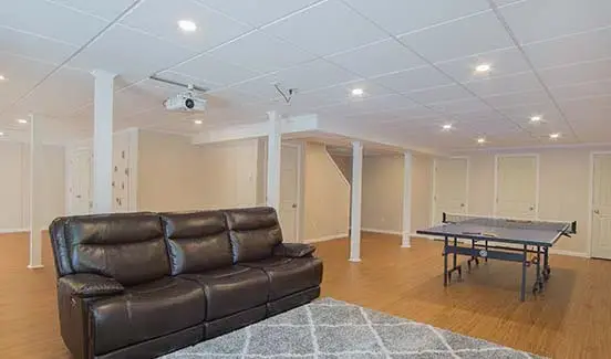 Bright open-plan basement remodel with leather couches, ping pong table, and projector screen