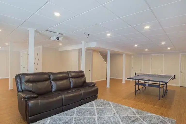 Renovated open-plan basement with leather couch and ping pong table. Light wood floors, recessed lighting.
