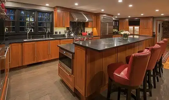 Kitchen with black-trimmed windows, black marbled backsplash, wooden cabinetry, and stainless steel accents