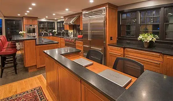 Kitchen with black-trimmed windows, black marbled backsplash, wooden cabinetry, and stainless steel accents