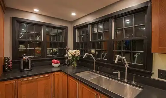 Kitchen with black-trimmed windows, black marbled backsplash, wooden cabinetry, and stainless steel accents