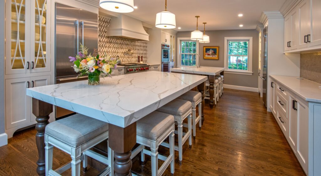 upgraded modern kitchen remodel with wood floors, white cabinets, and two large islands with woodgrain table legs and white marble countertop.