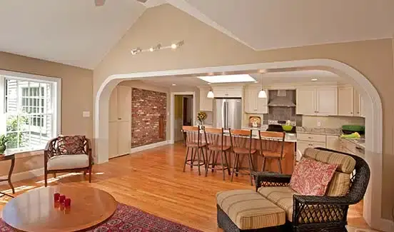 Renovated home addition with large open doorway from kitchen with island to living area. Wood floors. Light tan walls. Track lighting