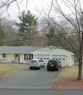 Yellow vinyl family home with two garages and two cars in the driveway