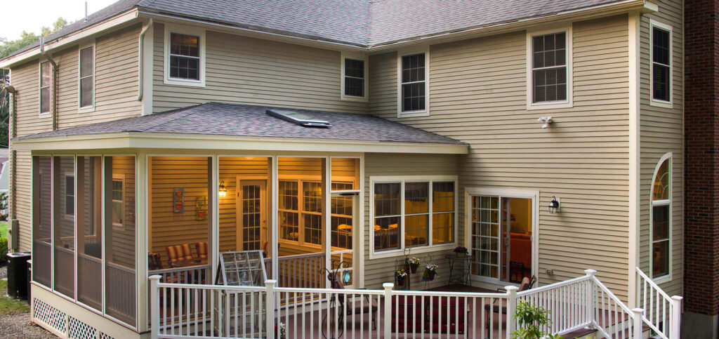 A custom-built patio deck with screened-in portion on back of a two-story beige home.