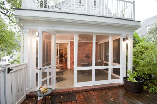 View of a screened-in porch remodel on a historic home, from a wood deck outside, with trees surrounding.