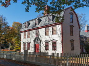 Historic two-story farmhouse-style home with white siding and red trim, three dormers, red front door.