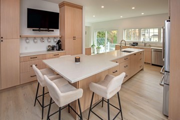 Minimalistic kitchen remodel with Scandinavian design. Long middle island with square countertop at one end, with stool seating around it. Sink at other end.